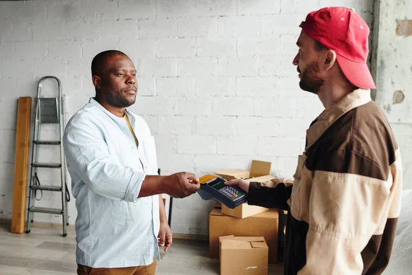 アフリカの男性のクライアントがクレジットカードで読み込みとサービスを提供するために支払う間 作業服保持端末の若いローダー — ストック写真