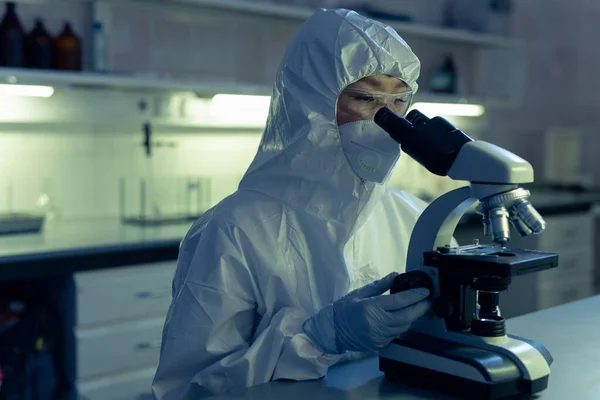 女化学家穿着防护工作服 戴着面具 在实验室工作时透过显微镜观察 — 图库照片