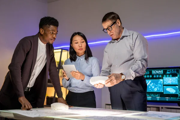 Modern ofiste masada duran ve tablet ve maketi kullanarak 3D araba modelliği yapan dalgın çok ırklı meslektaşlar.