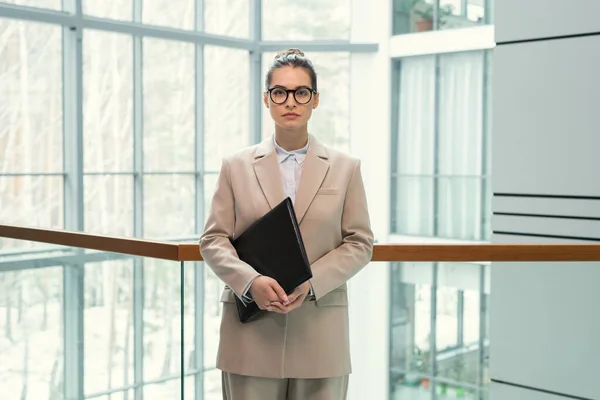 Portret Poważnej Atrakcyjnej Bizneswoman Okrągłych Okularach Stojącej Czarnym Folderem Lobby — Zdjęcie stockowe