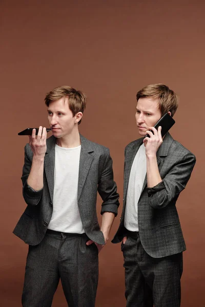 穿着灰色西装的自信的现代人站在棕色背景下 用智能手机进行交流 — 图库照片