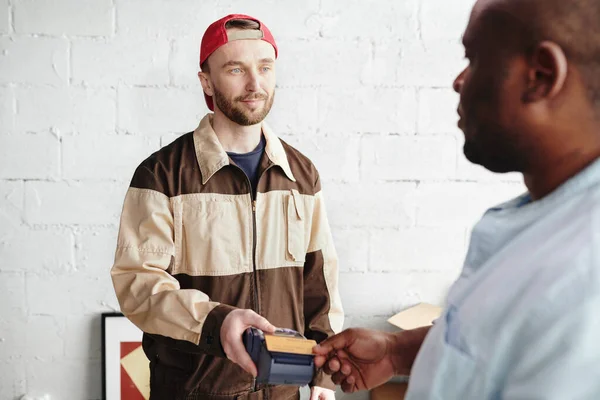 労働者の若者が支払端末を保持し アフリカの男性のクライアントを見てクレジットカードでサービスをロードして提供するために支払う — ストック写真