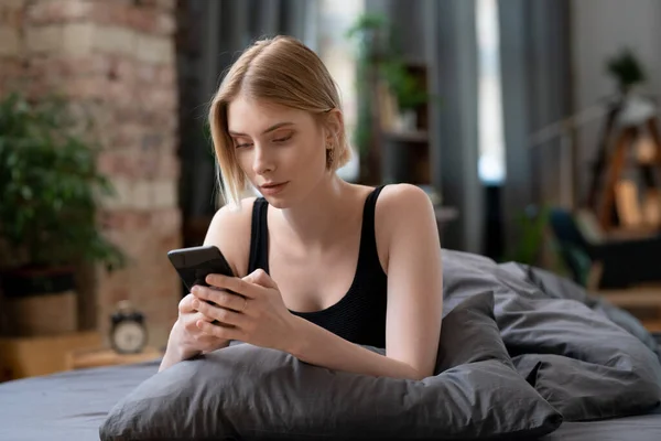 Genç Sarışın Kadın Sabah Yatağında Otururken Internetteki Işlerinde Cep Telefonu — Stok fotoğraf