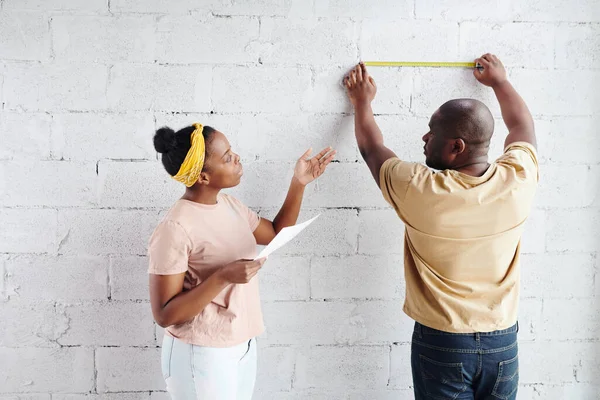 站在丈夫身边的非洲青年妇女 一边测量墙砖的长度 一边在整修房屋时与他协商 — 图库照片
