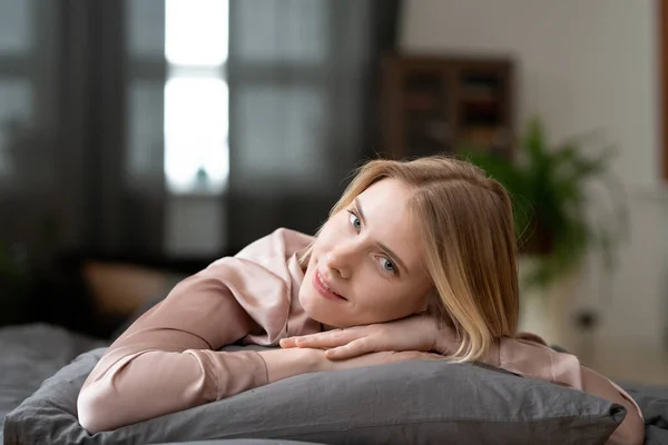 Genç Sarışın Kadın Yastığa Uzanıyor Yatak Odasında Dinlenirken Kameraya Bakıyor — Stok fotoğraf