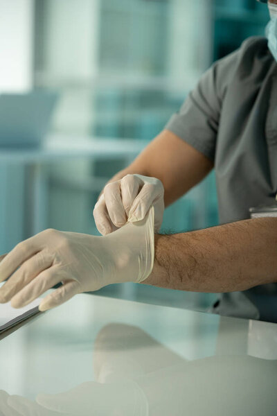 Close-up of unrecognizable medical researcher sitting at table and putting gloves on hands