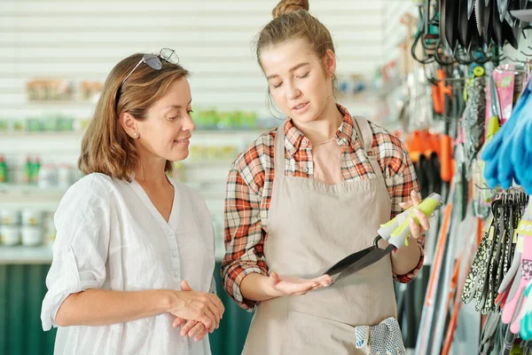 Feliz Joven Asistente Tienda Jardinería Delantal Camisa Mostrando Pequeñas Palas — Foto de Stock