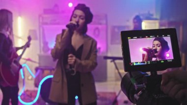 Gece kulübünde rock konseri veren müzik enstrümanları çalan bayan meslektaşları mikrofon içinde şarkı söyleyen çekici solistin yakın plan çekimleri.