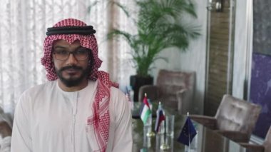 Genç BAE dışişleri bakanının belden aşağısı ağır ağır portresi modern müzakere odasında duran kameraya bakıyor