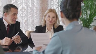 Over-the-shoulder waist-up shot of male and female business company representatives discussing contract details sitting together at negotiation table