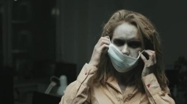 SFX makyajlı, dağınık saçlı, yüz maskesi takmaya çalışan zombi kadının portresi.