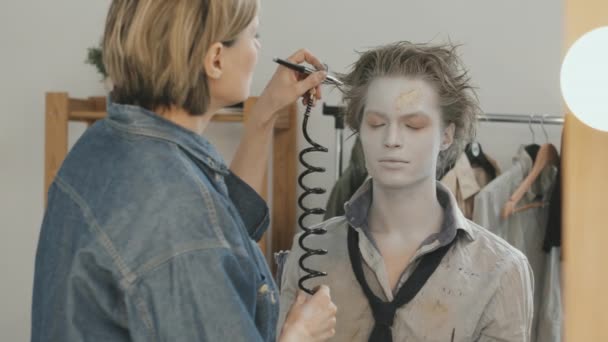 女性Sfx艺术家的Slowmo Pan应用喷枪机对有假肢疤痕的男演员面部进行白化处理 — 图库视频影像