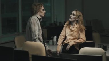 SFX makyajlı, yırtık elbiseli, homurdanan zombi adam ve kadının karanlık ofiste konuştuğu orta boy bir fotoğraf.