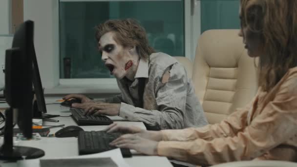 コンピュータで作業しようとしている間 心のない男性と女性のゾンビのスローモーションで撮影されたSfxメイクと机の上に座って汚い服を引き裂き キーボードとマウスに手をスマッシュ — ストック動画