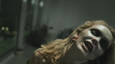 SFX makyajlı, lekeli dişli, homurdanan ve kameraya doğru yürüyen kızgın zombi kadının yakın çekim görüntüsü.