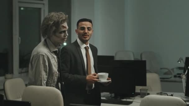 Pan拍摄的商人身穿西服 手里拿着咖啡 一边和僵尸办公室的工作人员说话 一边和他一起走在桌子之间 — 图库视频影像