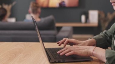 İki çocuğu arka planda video oyunu oynarken, orta bölüm PAN ağır ağır dizüstü bilgisayar başında çalışan modern kadın.