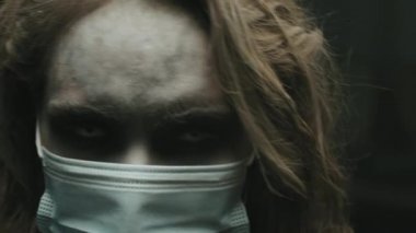 Beyaz lensli, maske takan ve kameraya bakan zombi kadını yakından çek.