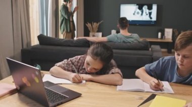 Anneleri telefonda konuşurken ve babaları arka planda televizyonda hokey maçı izlerken, kız ve erkek kardeşlerinin internet üzerinden kitap yazılarının PAN belden yumağı fotoğrafı.