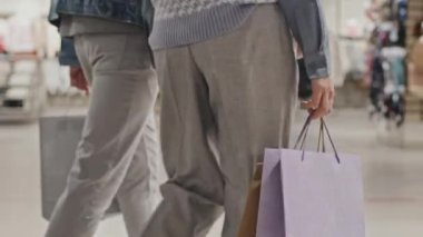 Elbise mağazasında elinde alışveriş çantalarıyla gezen, modaya uygun örülmüş geniş paçalı, tanınmayan bir kadının düşük kesiminden bir fotoğraf.