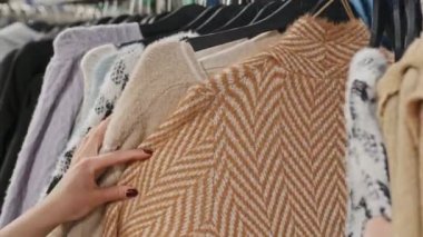 Modern giyim mağazasının örgü bölümündeki raylarda asılı pastel ve bej renkli süveterleri sınıflandıran tanınmayan kadınların yakın çekimi.