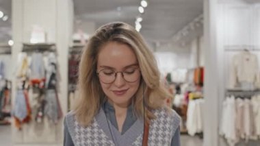 Moda kıyafetler ve aksesuarlar giyen genç bir kadının, büyük modern giyim mağazasında bir sürü alışveriş çantası taşıyan eşyalara baktığı bir fotoğraf.