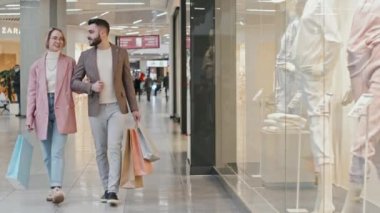 Modern alışveriş merkezlerinde vitrin vitrinlerinde kameraya doğru yürürken bir sürü alışveriş çantası taşıyan şık bir çiftin fotoğraf çekimi.
