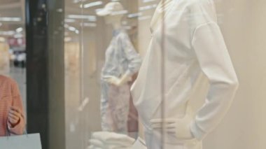 Yüzü maskeli genç beyaz bir kadının büyük bir alışveriş merkezinde kıyafet alışverişi yaparken, vitrinlerdeki giyim mağazaları vitrinlerine bakarken çekilmiş belden yukarı pozu.