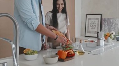 Modern minimalist tarzı mutfakta sebze salatası yaparken genç Latin çiftin orta boy havadan çekilmiş görüntüsü.