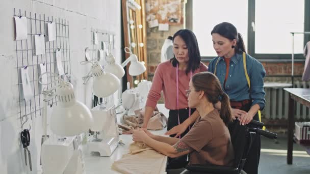 与女时装设计师交谈的轮椅女裁缝和工作室缝纫服装的中景照片 — 图库视频影像