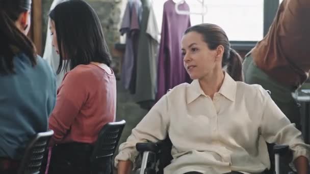 坐在轮椅上与在工作室做衣服的快乐女裁缝交谈的中景照片 — 图库视频影像