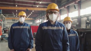 Fabrika yöneticisinin orta boy portresi ve iş yerinde solunum maskesi takan, kameraya poz veren iki erkek ve kadın çalışan.