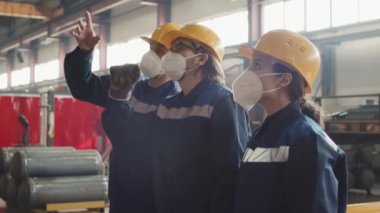 Yeni erkek ve kadın işçilerin fabrikada nasıl makine kullanacaklarını, herkesin solunum maskesi, şapka ve üniforma taktığını açıklayan orta derecede yavaş bir erkek denetleyici.