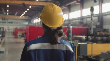 Dikiz ayarı, çalışanların çalışmalarını kontrol eden fabrika tesisinde yürüyen kasklı ve üniformalı kadın yöneticinin yavaşlığını takip ediyor.