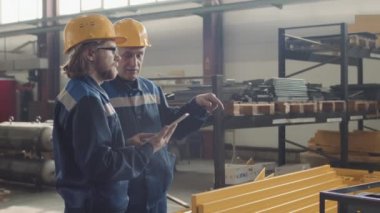 Yetişkin erkek bitki yöneticisinin tabletli işçiyle konuşurken orta boy el kol hareketi yapması ve ileriye bakması.