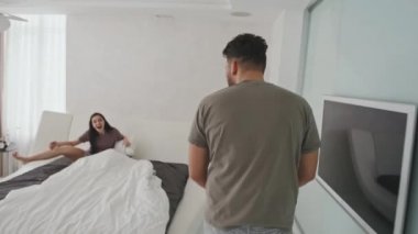 Orta boy, neşeli, genç Latin çiftin evde birlikte eğlenip yatakta yüksek sesle gülerken çekilmiş bir fotoğrafı.