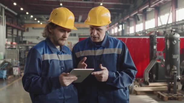 Medium Traagheid Van Twee Mannelijke Fabrieksarbeiders Harde Hoeden Uniformen Bespreken — Stockvideo