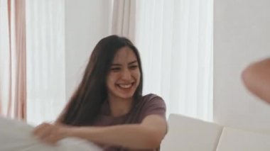 Orta boy, uzun siyah saçlı, gülen bir kadının Latin erkek yastığıyla yatakta kavga edişinin fotoğrafı.