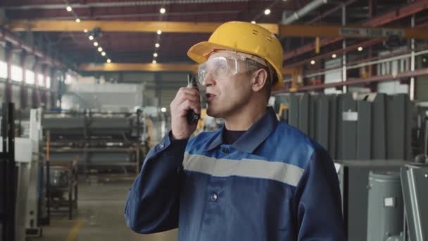 戴着安全眼镜 头戴硬礼帽 身穿制服的成人工厂主管的中型慢速给员工使用对讲机的指示 — 图库视频影像