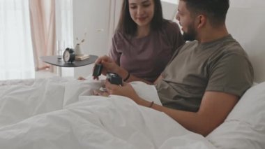 Heyecanlı bir Latin erkeğin, içinde pozitif hamilelik testi bulunan kutuyu açarken, genç ve mutlu bir eşle yatakta otururken ve birbirlerine nazikçe sarılırken orta boy çekimleri.