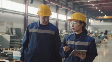 Dijital tabletli kadın yöneticinin orta yavaşlığı yeni işçiyle konuşuyor. Güvenlik gözlükleri ve sert şapkalarla tesiste yürürken makineleri nasıl kullanacağını anlatıyor.