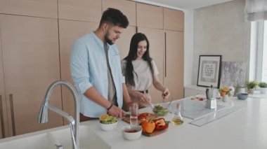 Modern mutfakta yemek pişirirken orta karar genç Latin ya da İspanyol çiftin konuşmaları, salata için sebze kesmeleri.