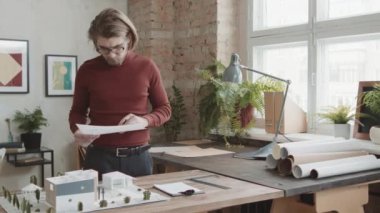 Kafkas sakallı bir mimarın modern tasarım ofisinde masa düzeni üzerinde çalışırken çekilmiş orta PAN resmi. Duvarlarda soyut resimler var.