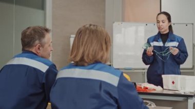 Orta büyüklükteki kadın denetçiyle birlikte çekilen PAN, işçilere oksijen maskesi kullanımını gösteren endüstriyel tesislerdeki güvenlik önlemleri hakkında talimatlar veriyor.