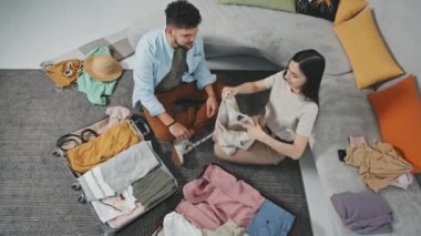 Modern dairelerinin zemininde oturan ve tatile gitmeden önce bavullarını toplayan genç çiftin en iyi görüntüsü.