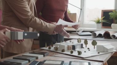 Üç erkek ve kadın mimarın göbek kısmındaki yavaşlama, ofisteki 3D yapısını inceleyen modern iki katlı ev inşaatında birlikte çalışıyor.