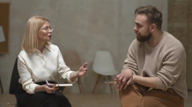 Kadın psikolog ve depresyondaki adamın ruh sağlığı merkezinde oturup konuştuğu orta boy bir fotoğraf.