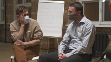 Grup terapi seansında ruh sağlığı veya bağımlılık sorunları hakkında konuşurken yüz maskesi takmış iki depresyonlu adamın orta boy fotoğrafı.