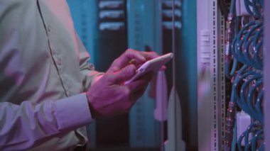 Tablet üzerinde yazan ve sunucu odasındaki bilgisayar ekipmanlarına bakan orta yaşlı erkek veri merkezi çalışanını yakın çekime al