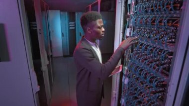 Veri merkezinin sunucu odasındaki tablet kontrol sunucuları veya diğer bilgisayar ekipmanlarıyla genç Afro-Amerikalı erkek teknisyenlerin görüntüsü.